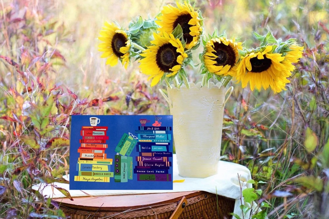 Image of a blue notecard on a picnic basket. There are sunflowers beside it. The notecard features a rainbow of book spines, each by a Black woman author. 