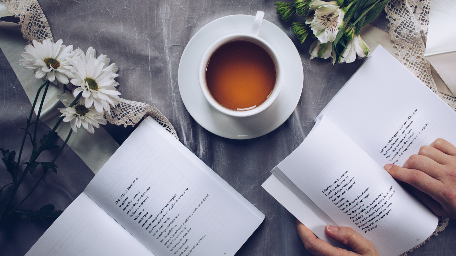 a photo of someone reading a poetry book with flowers and tea