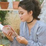 a lighter-skinned Asian woman reading by some potted plants