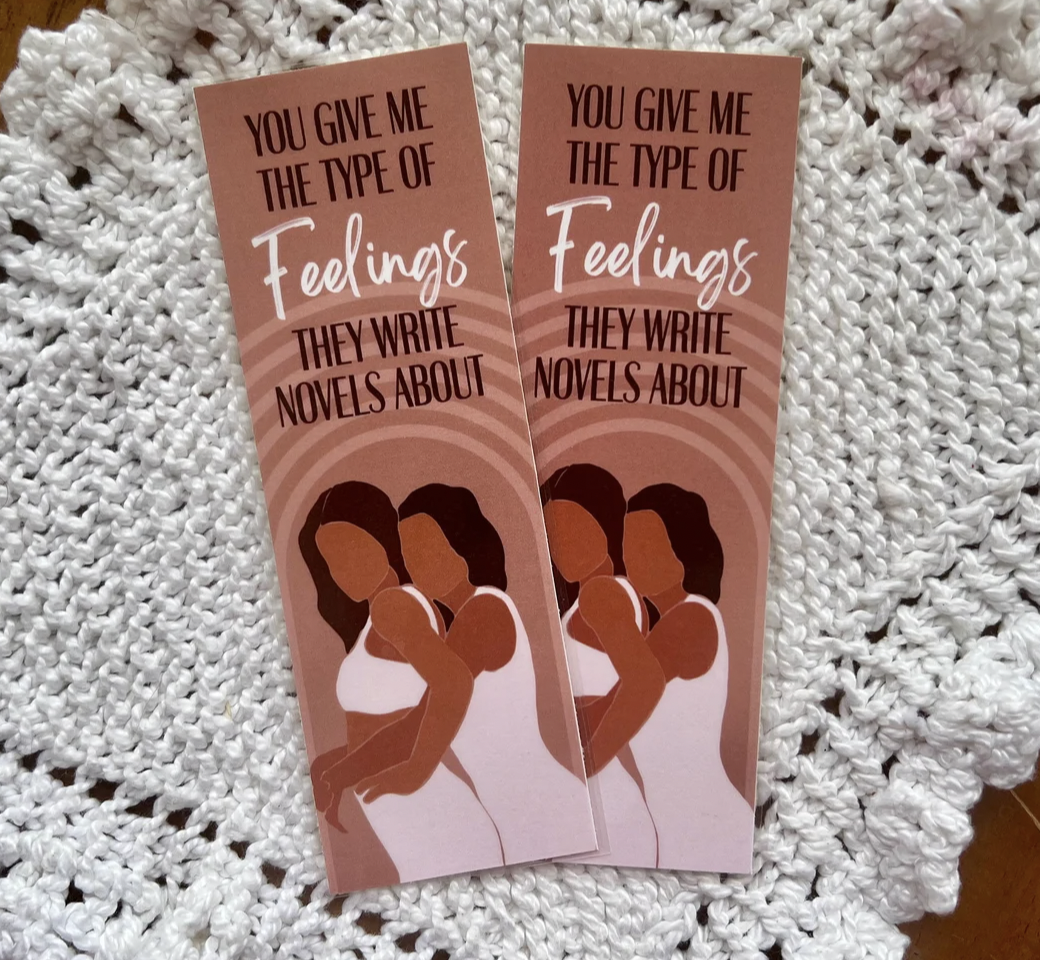 Image of two bookmarks with illustrations of two Black femmes embracing and the words "You give me the type of feelings they write novels about"