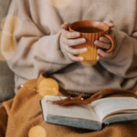 a person wearing a sweater and holding a mug with an open book in their lap