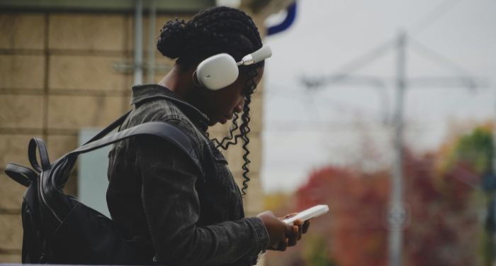 Image of a Black woman with headphones and holding an iphone.